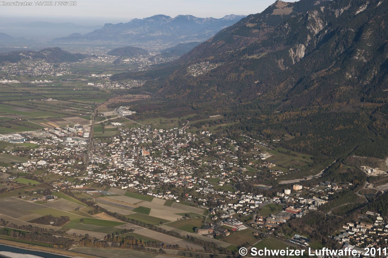Liechtensteiner Rheintal, Schaan (Position 2'757'154.67, 1'226'027.41) im Bildzentrum. Blick nordwärts. Maiensäss am Hang (Bildmitte): Planken, darunter gelegen im Tal: Nendeln. weiter nordwärts: Mauren. Am linken Bildrand oben: Eschen.